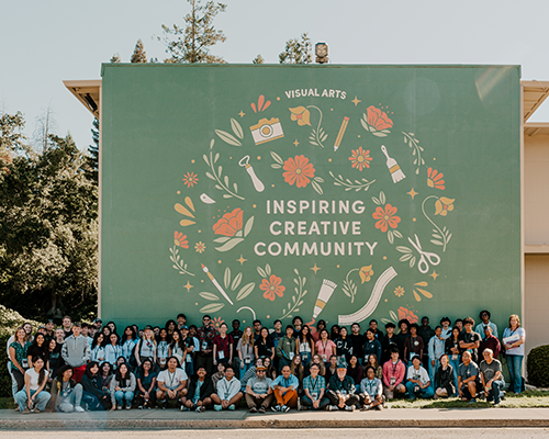 Several students in front of a green sign reading "Visual Arts: Inspiring Creative Community"