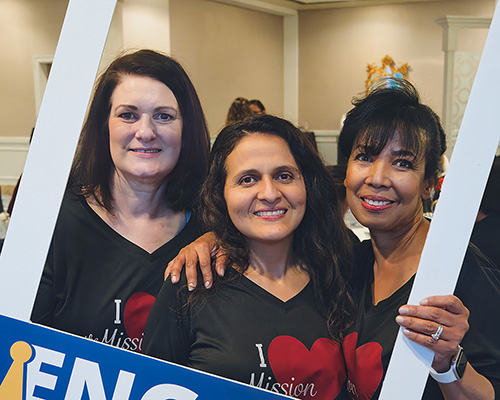 three women of different ethnicities in a cardboard frame reading "Engage"