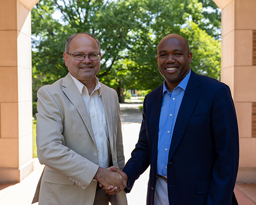 Two men of different ethnicities smiling and shaking hands.