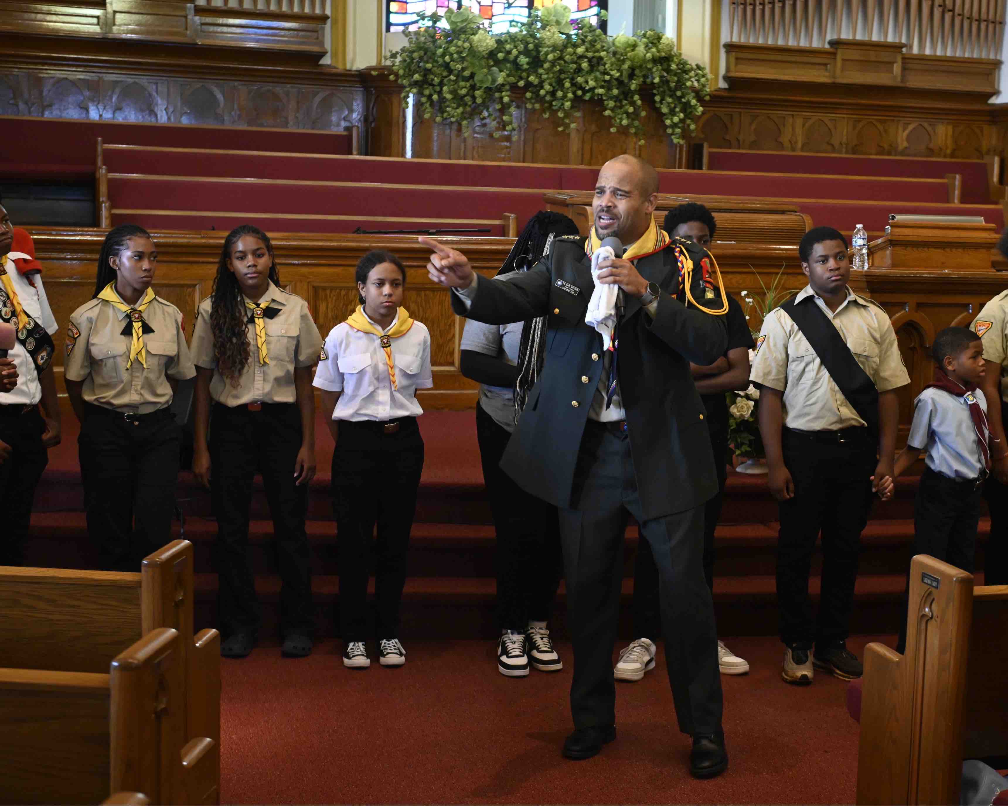 A pastor speaks in front of a church with young Pathfinders behind him