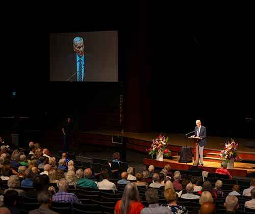 Older man on a stage stands in front of a crowd