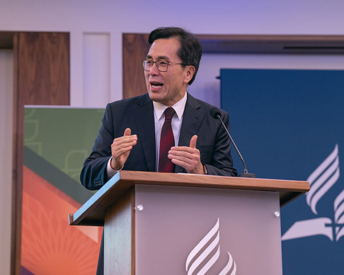 Kyoshin Ahn, a middle aged Korean man standing behind a pulpit with a microphone