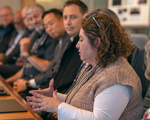  A woman speaks as men look on, all seated at a long table