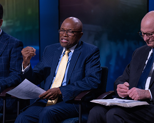 Closeup of two men in suits, one praying while the other listens