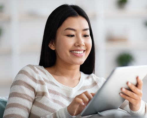 A smiling Asian woman looks at a tablet