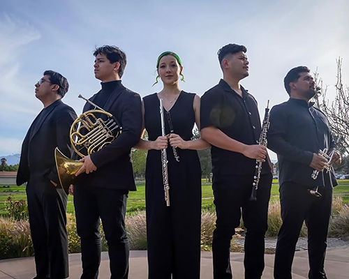 Four young men and a young women holding wind instruments in an outdoor group shot. 