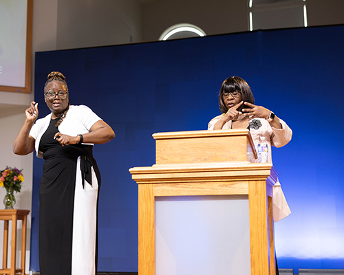 A woman does sign language interpretation for another woman standing behind a podium