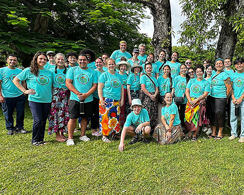 A diverse group in green t-shirts pose outside in Fiji. 