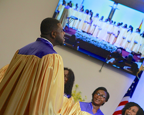 Close-up of Ghanaian choir wearing robes; screen showing fubacground. 