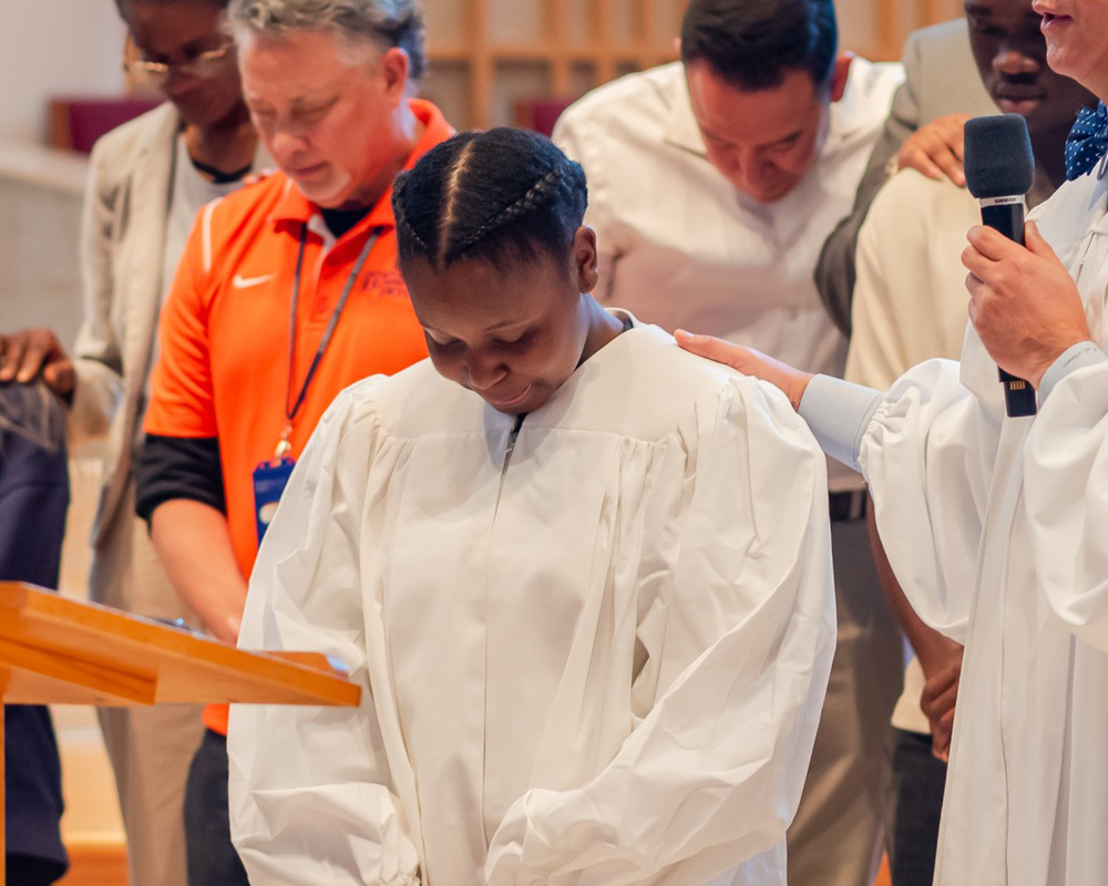 Young woman in a white gown prayed over by a pastor on a stage