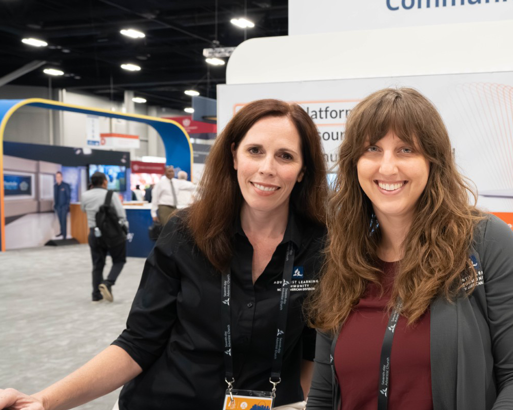 Two women pose at the Adventist Learning Center exhibit.