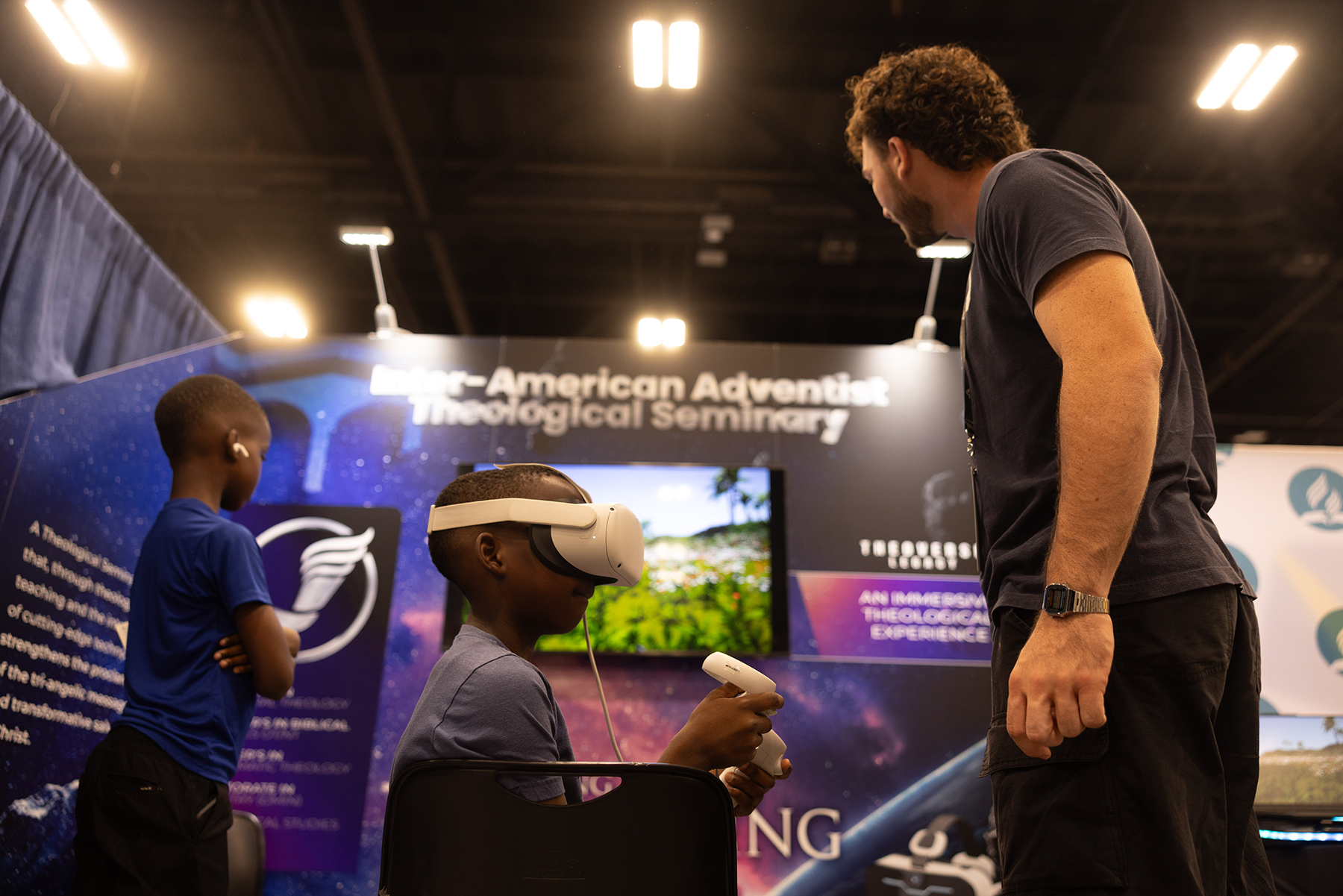 A young boy uses a virtual reality headset while an older man observes during the 62nd GC Session.