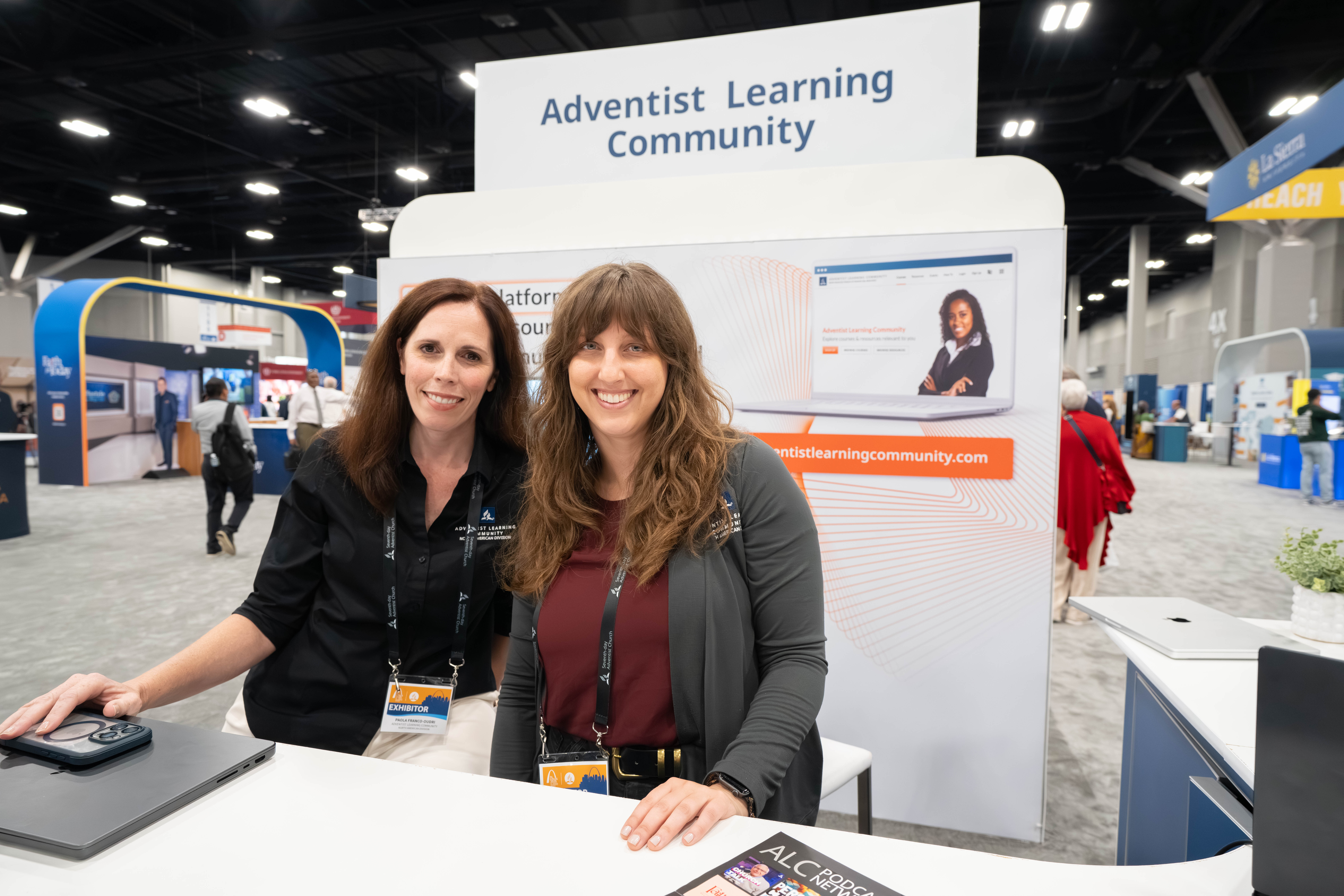 Two woman pose for a picture at the Adventist Learning Community Booth