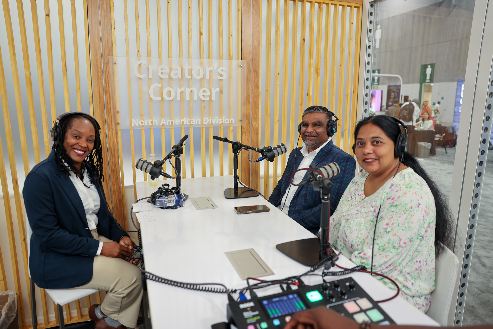 Three people sit together in the "Creator's Corner" studio space, recording with podcasting equipment. 