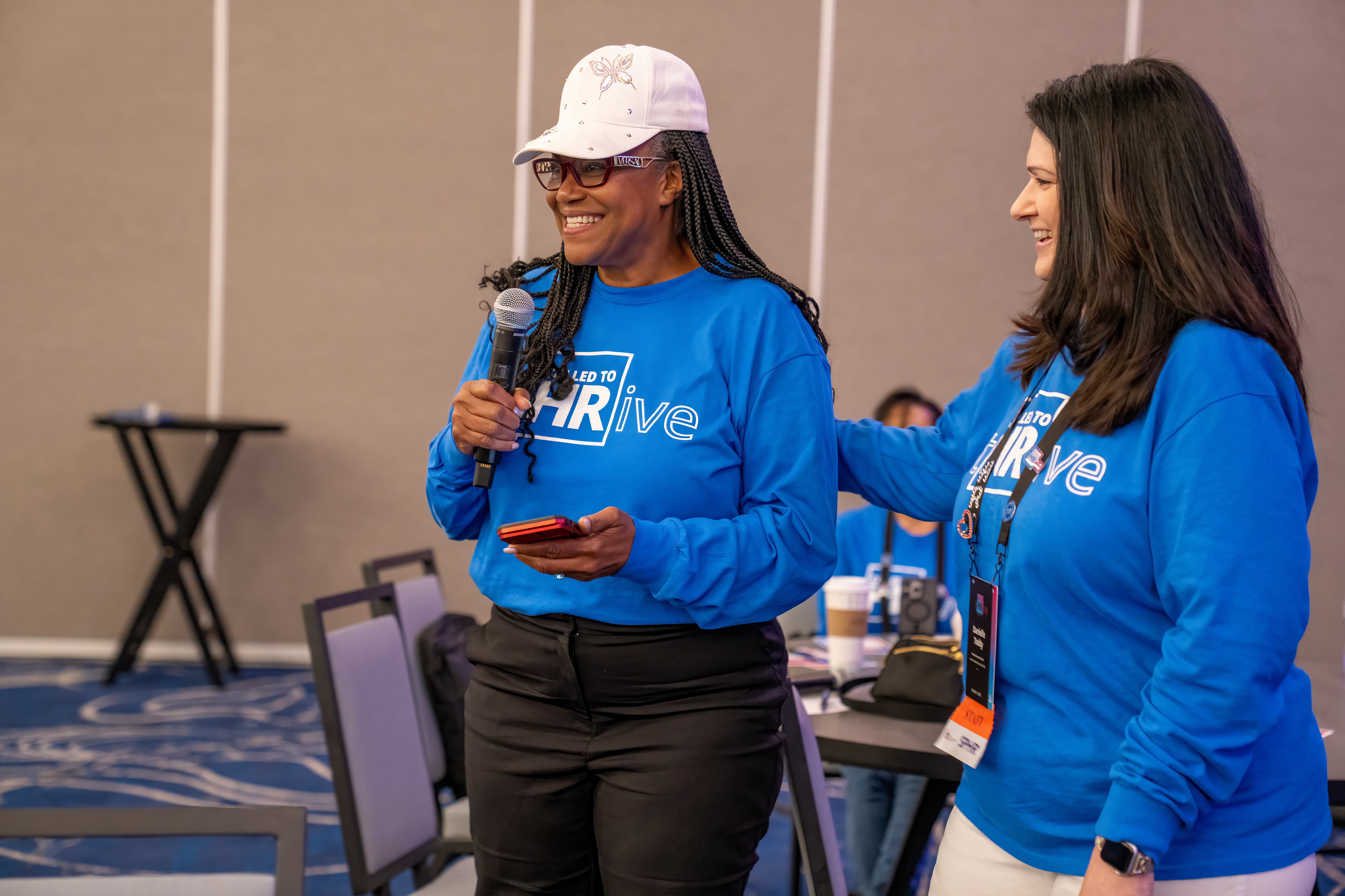 Two women smiling together, one holding a micropho