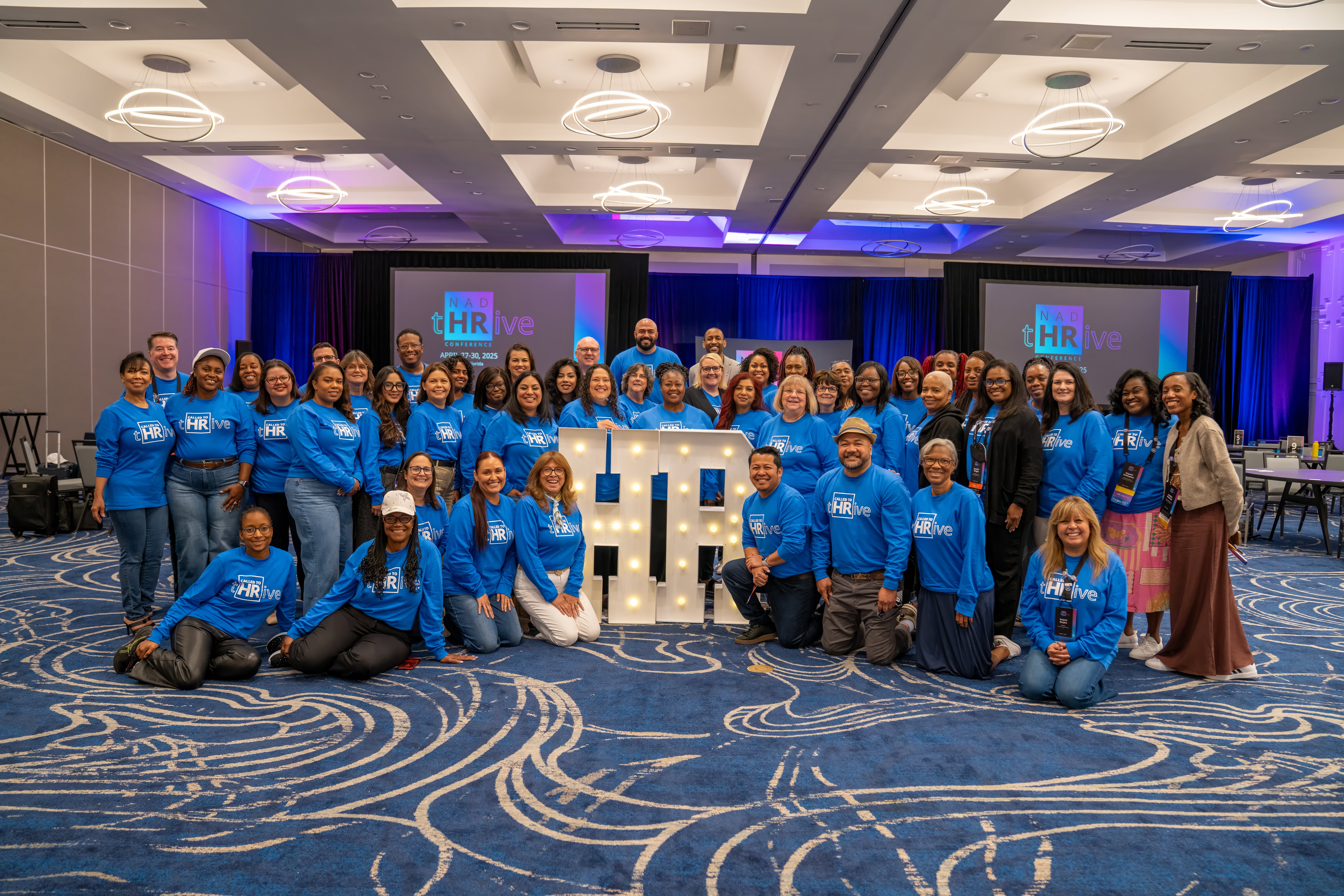 A diverse group of peopel smile with the NAD tHRive logo behind them
