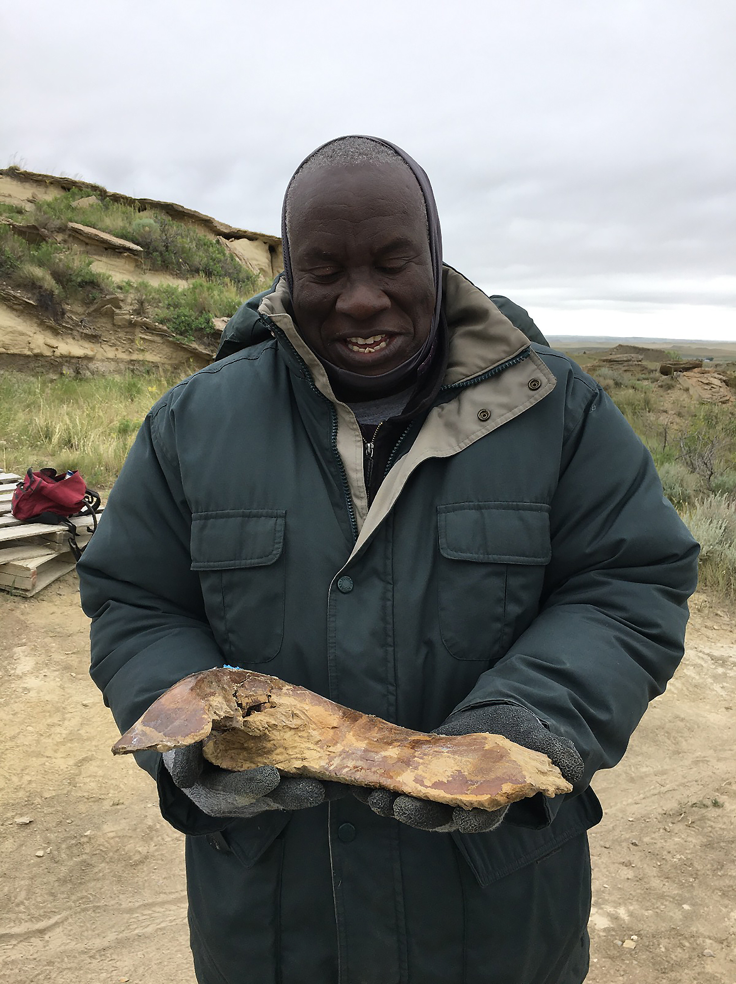 a smiling black man holding a bone on an excavation site