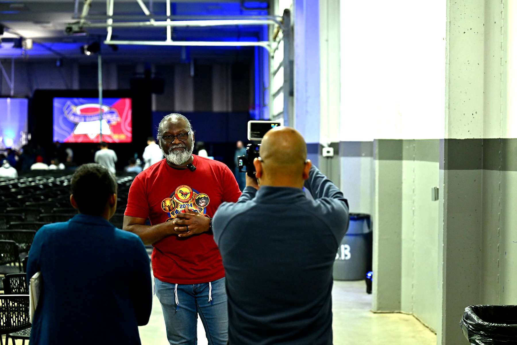 A black woman and Asian man, backs turned to the camera, interview a black man who is facing the camera.
