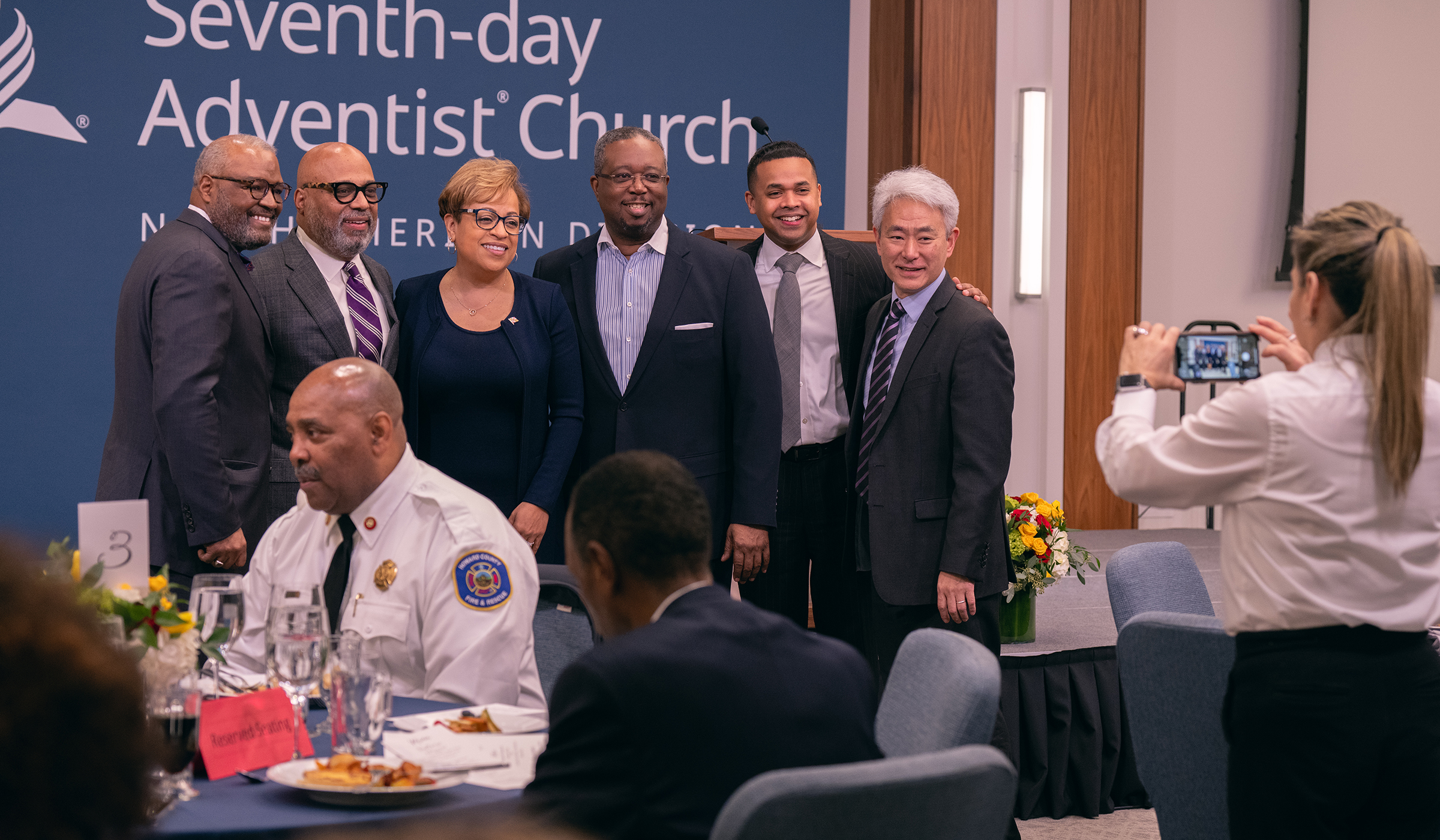 A photo of a small group of people of different ethnicities getting their photo taken at the front of a conference room. 