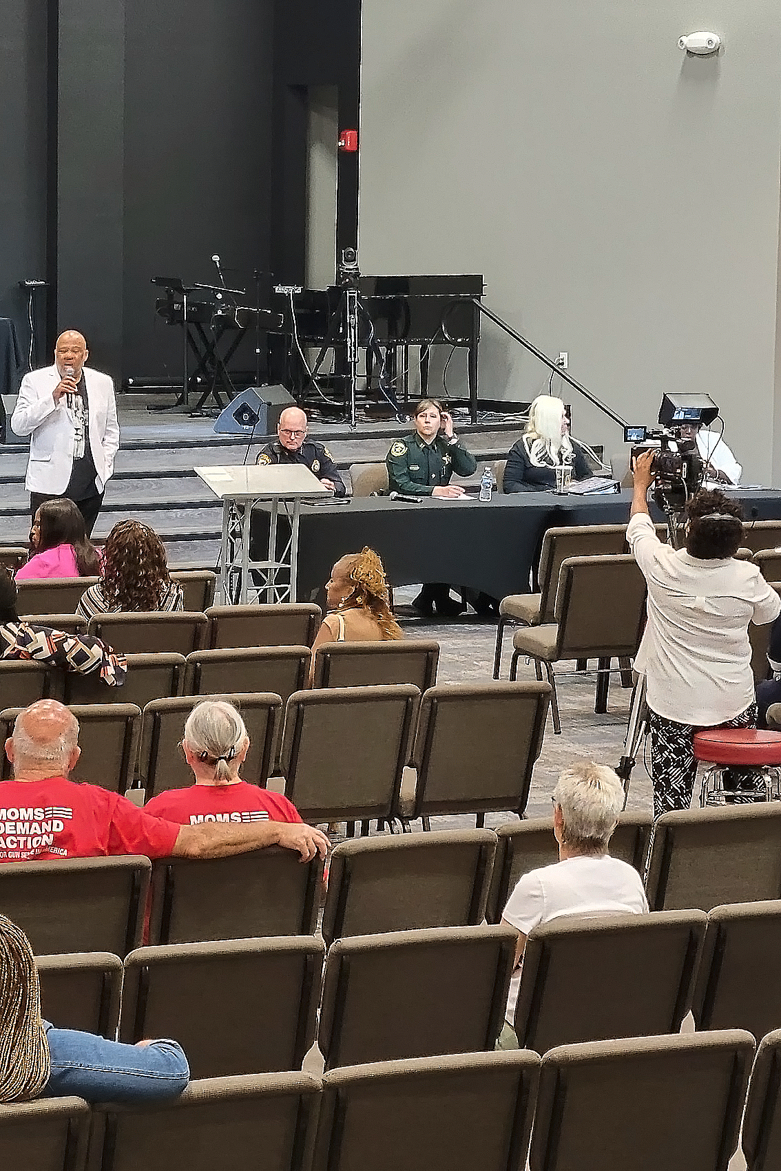 Black man stands in front of a crowd in an auditorium, speaking