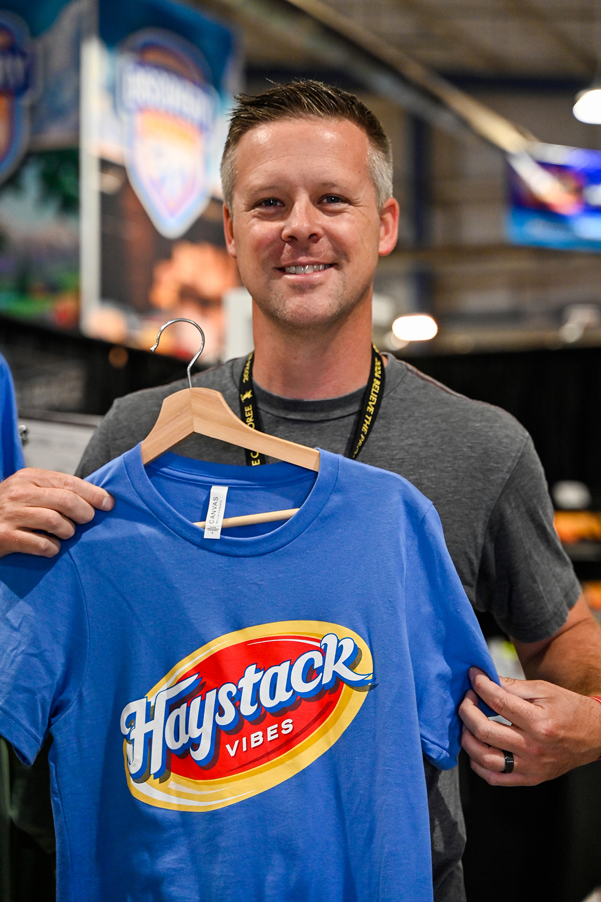 picture of a smiling man holding a shirt that reads "Haystack vibes."