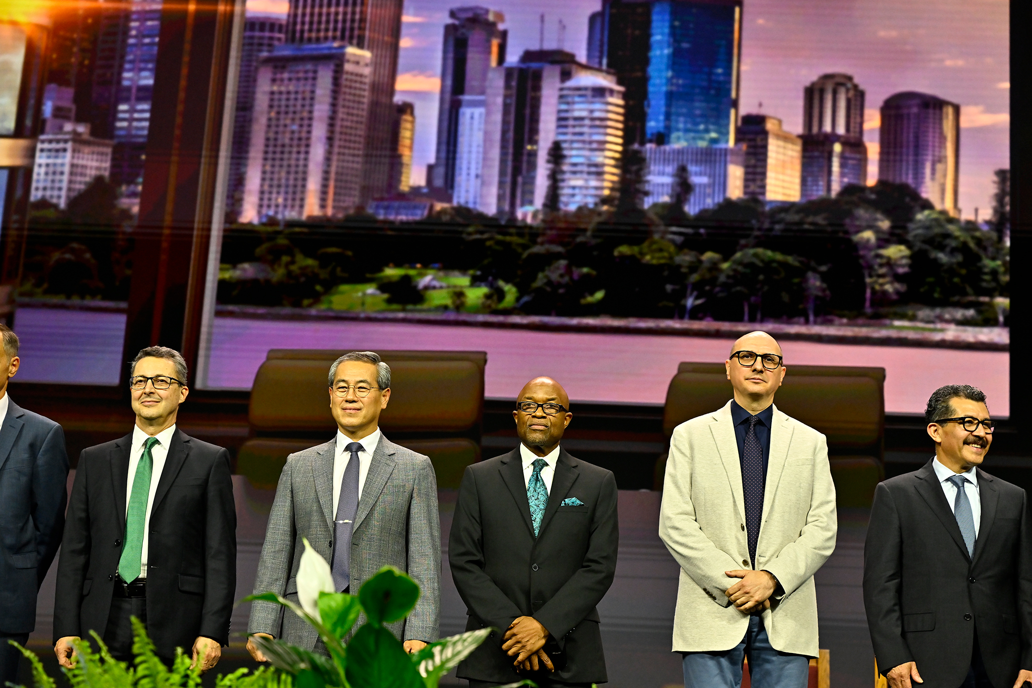 A diverse group of men in suits stand on a stage
