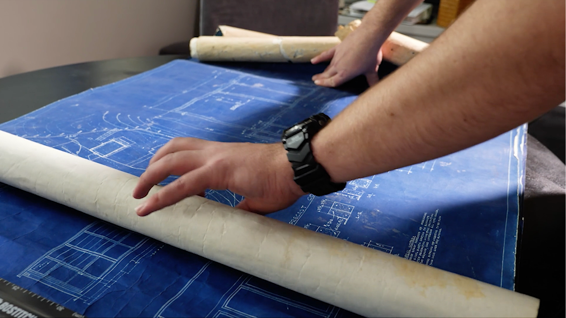 Screenshot of hands unrolling a blueprint.