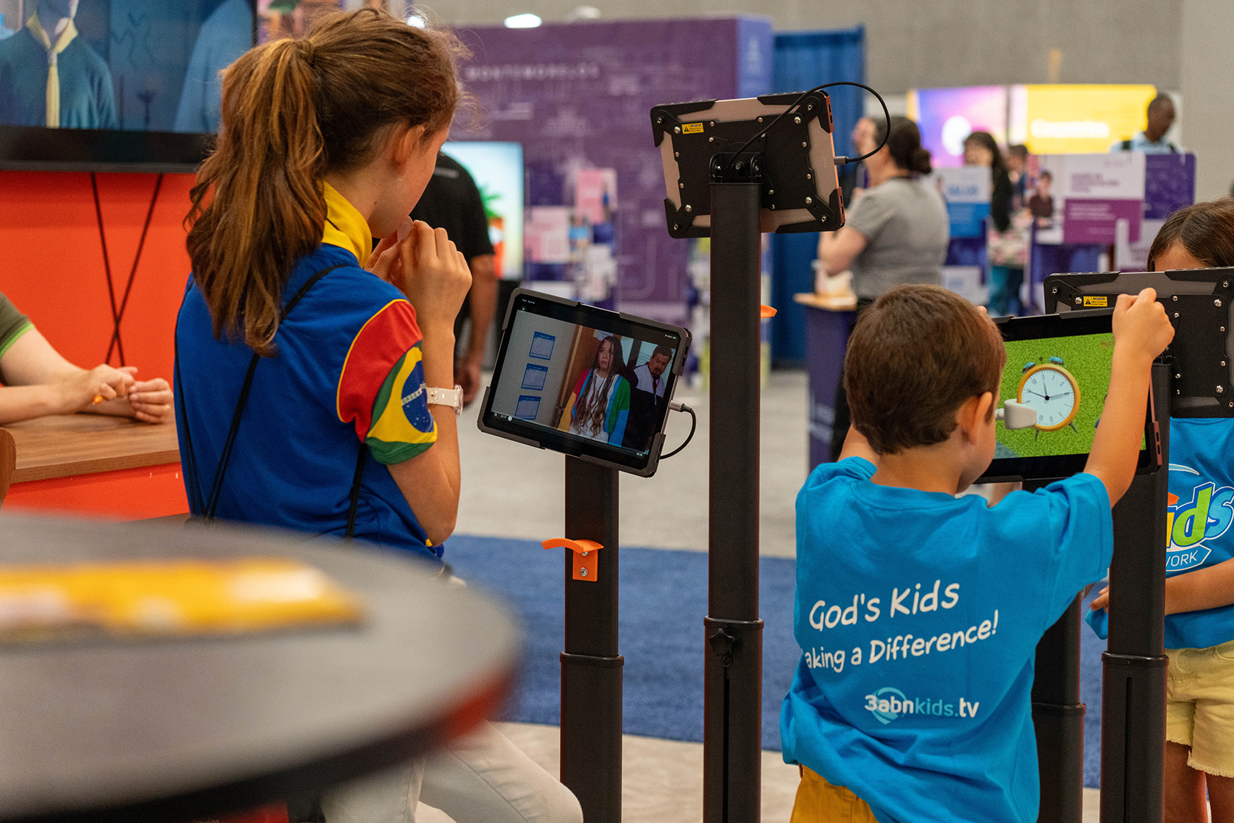 Boy and girl watch animated programs on iPads mounted on stands.