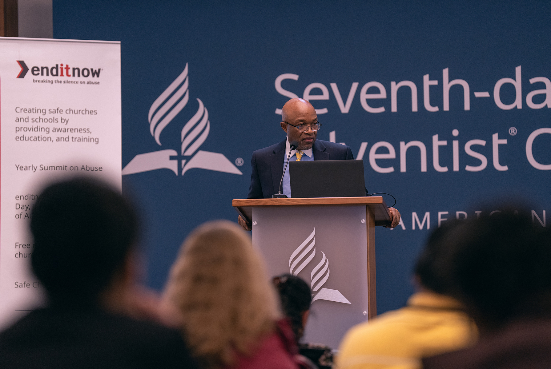Black man in suit speaks to crowd in an auditorium