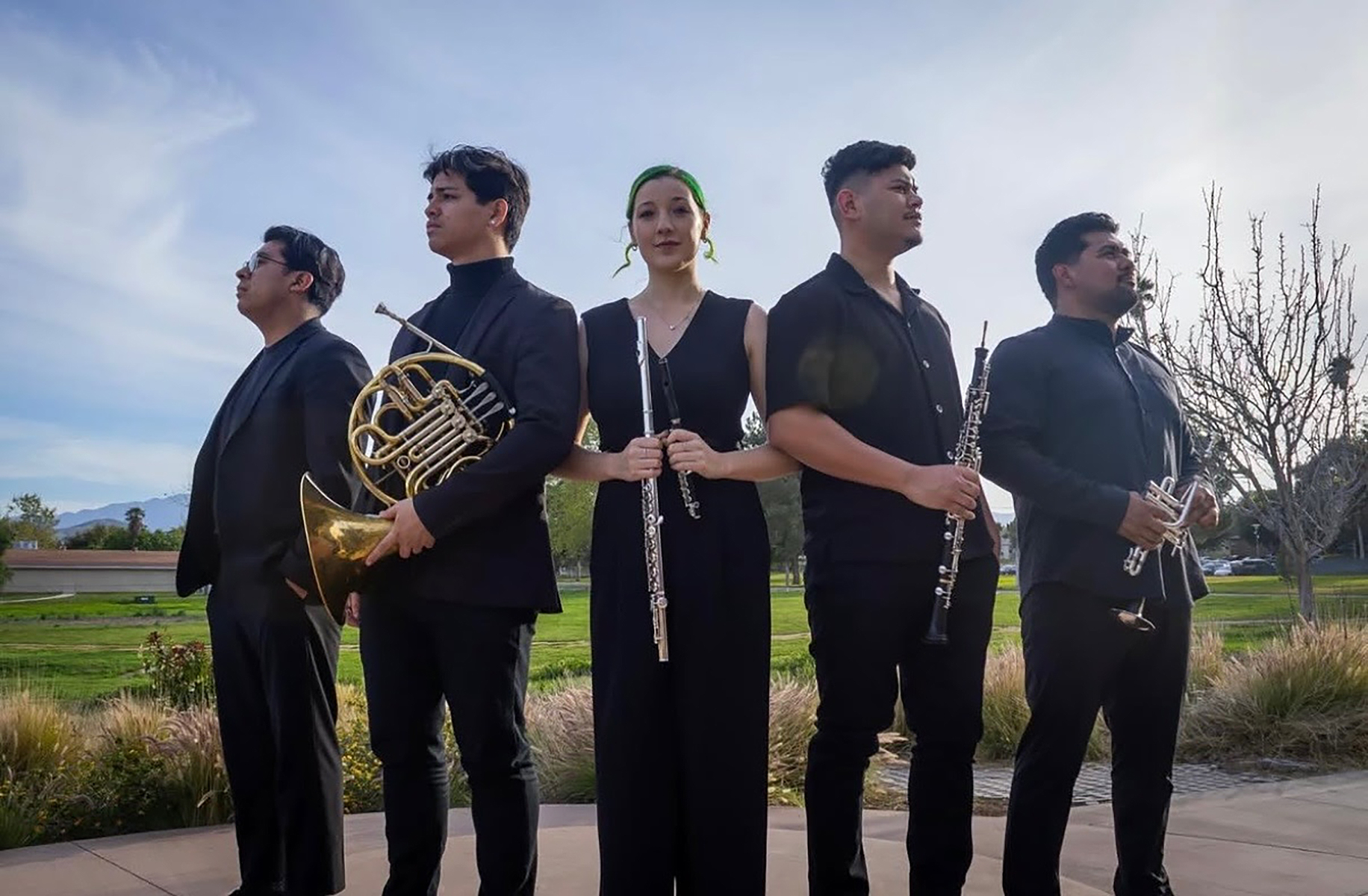 Four young men and a young woman holding different wind instruments in an outdoor group shot