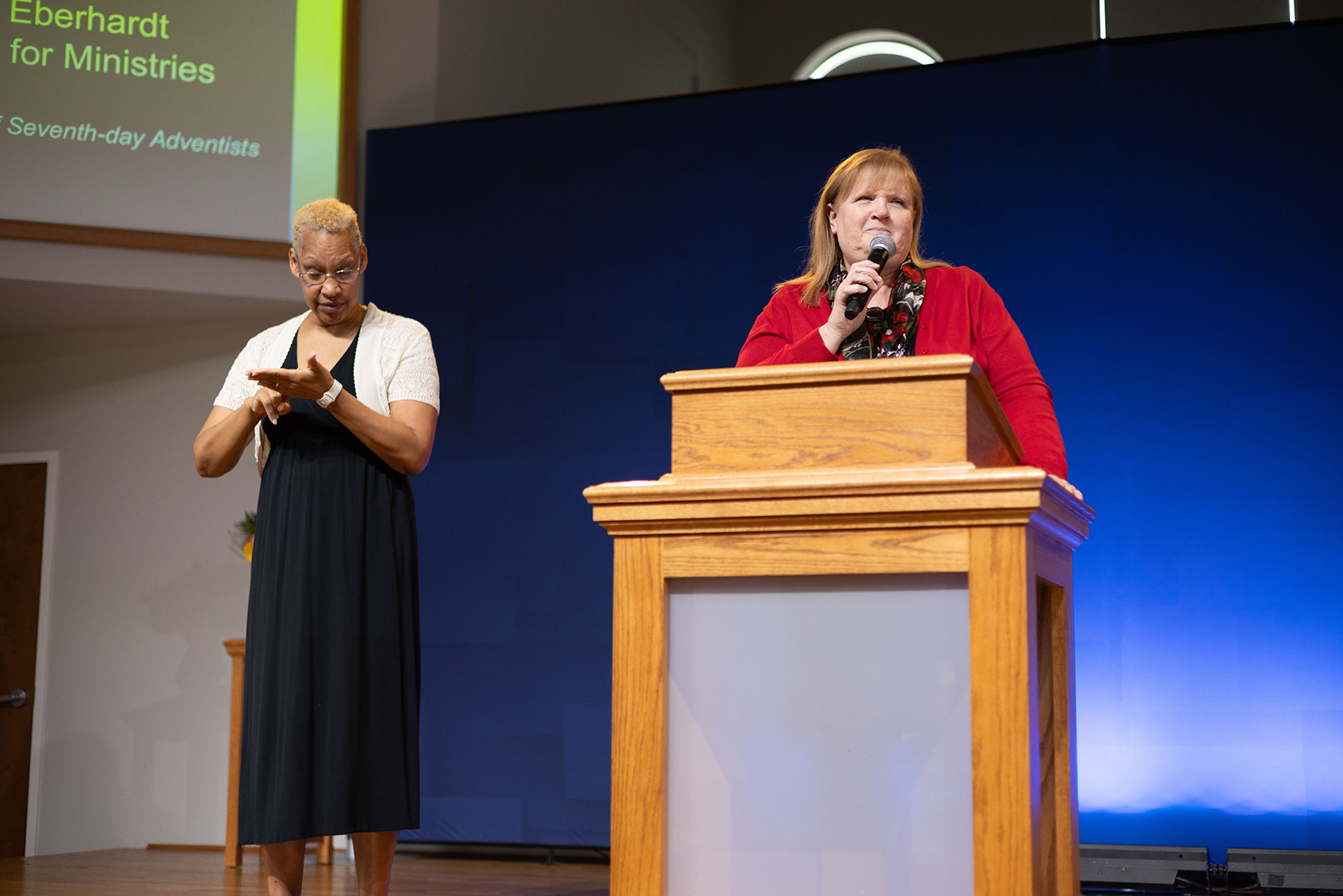 A woman does sign langauge interpretation for another woman speaking behind a podium