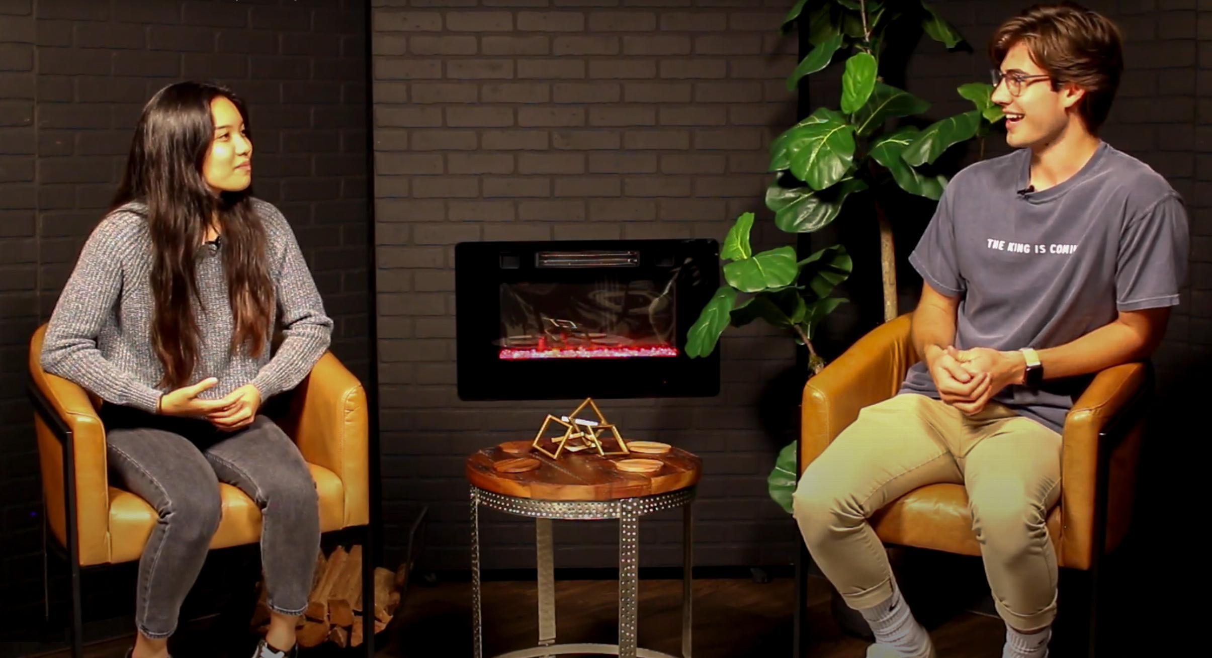 a young man and woman smiling and chatting together on a set of couches.