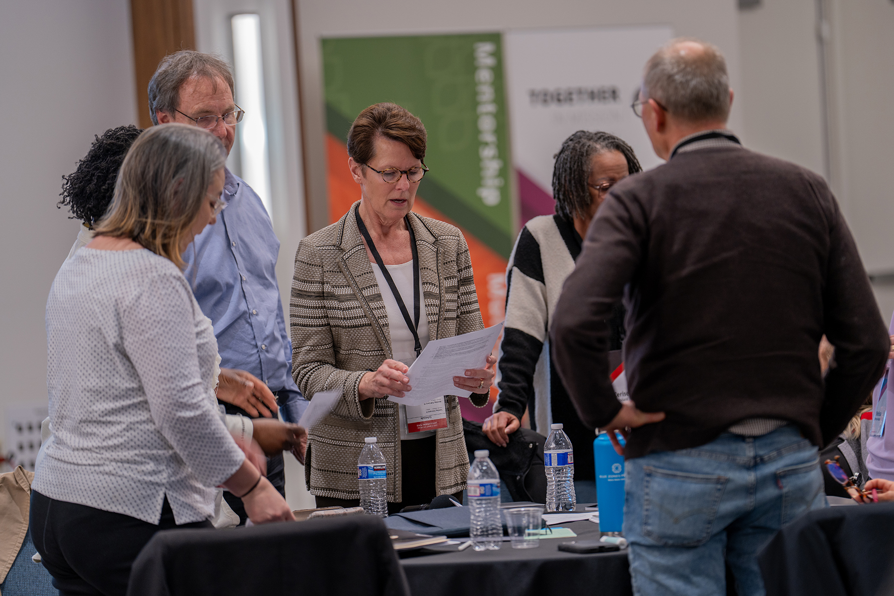 A diverse group of people standing up around a table. 