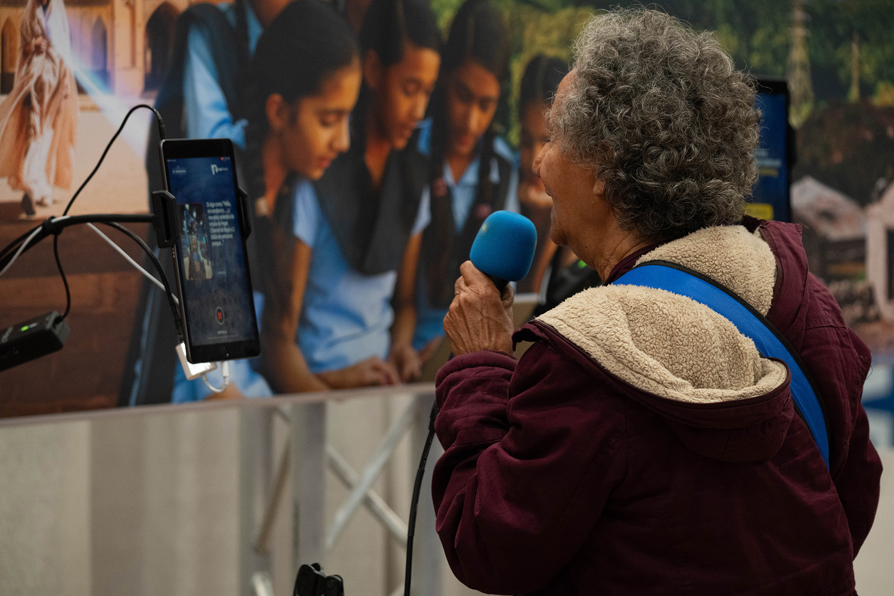 A woman speaks into a microphone, looking at a cell phone screen. 